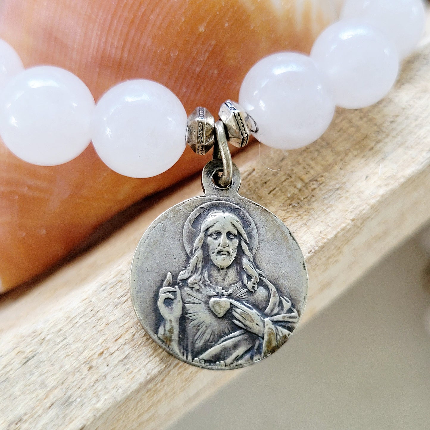 This 10 mm white jade beaded bracelet with silver medal of Our Sorrowful Mother holding Jesus on the front and The Sacred Heart of Jesus on the back.